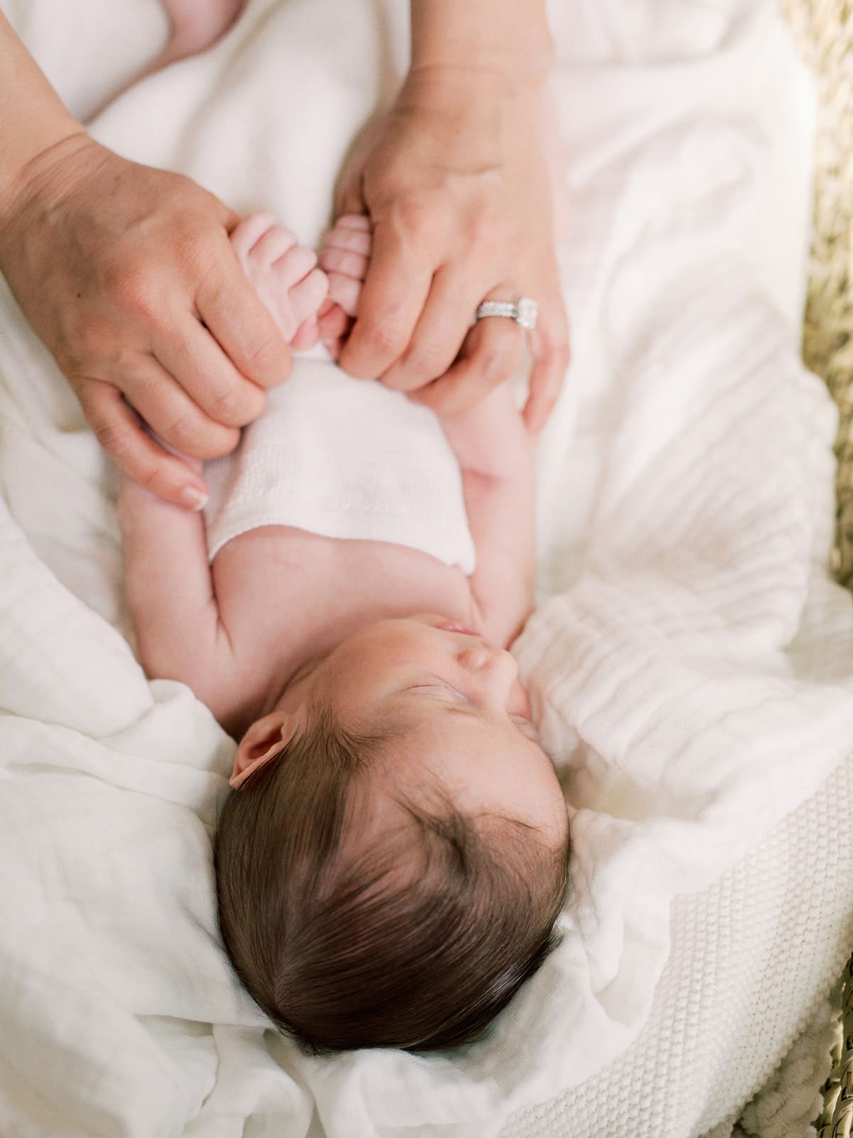 A newborn wrapped in a blanket and laying in a basket with his mother's hands holding his hands at a Richmond in-home newborn photography session by Katie Stansfield Photography.