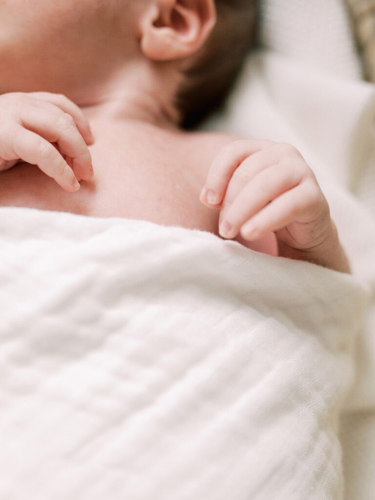 A close-up of a baby's hands while the baby is wrapped in a blanket during in-home newborn photos by Katie Stansfield Photography.