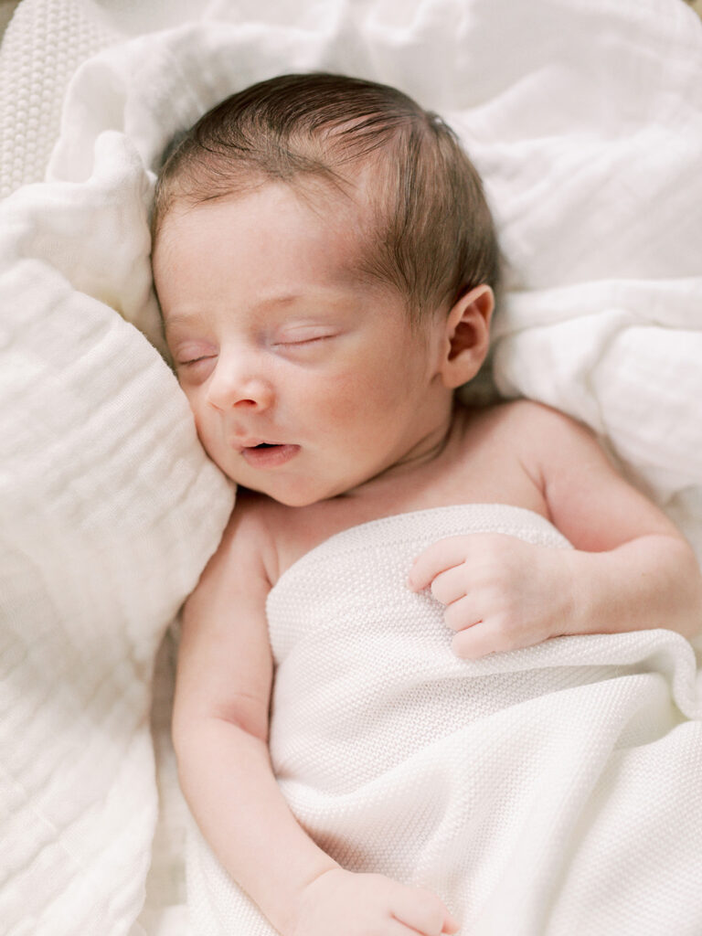 A baby sleeping while wrapped in a blanket and laying on a blanket during in-home newborn photos by Katie Stansfield Photography.
