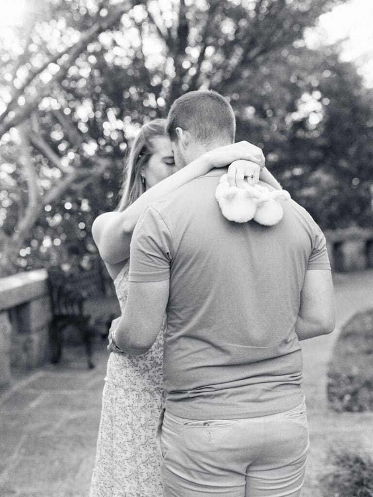 A man and woman touching foreheads while the woman holds baby slippers during a maternity photography in Virginia session by Katie Stansfield Photography.