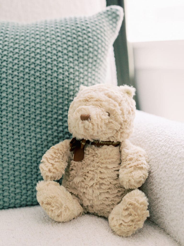 A stuffed bear and green crocheted pillow on a chair at a Richmond newborn nursery photography session by Katie Stansfield Photography.