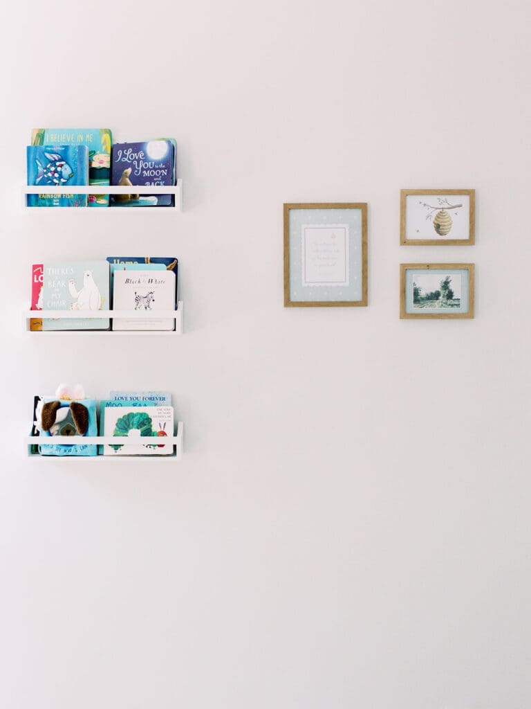 White book shelves with books and natural wooden framed prints on a wall at a Richmond newborn nursery photography session by Katie Stansfield Photography.