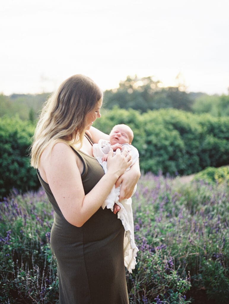 A mom standing in a garden as she looks at and holds her newborn during a Chesterfield newborn photography session by Katie Stansfield Photography.