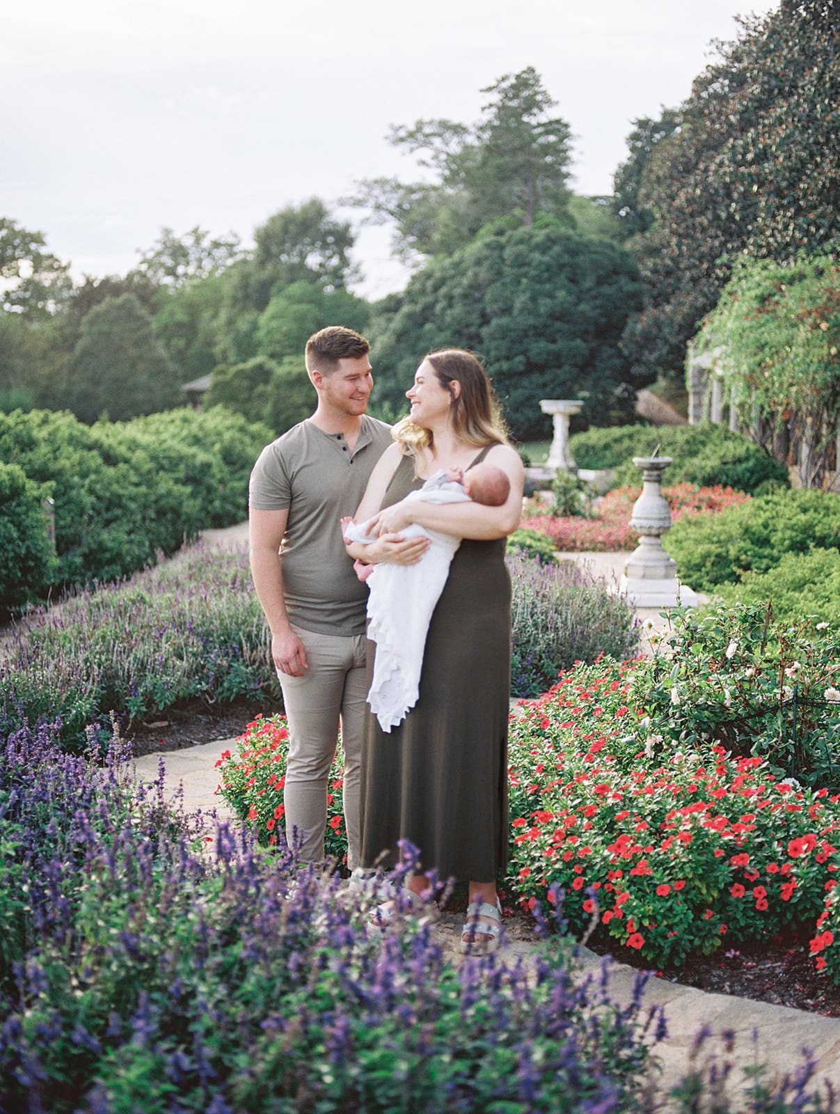 A mom and dad looking at each other in a garden as the mom holds their newborn during a Chesterfield newborn photography session by Katie Stansfield Photography.