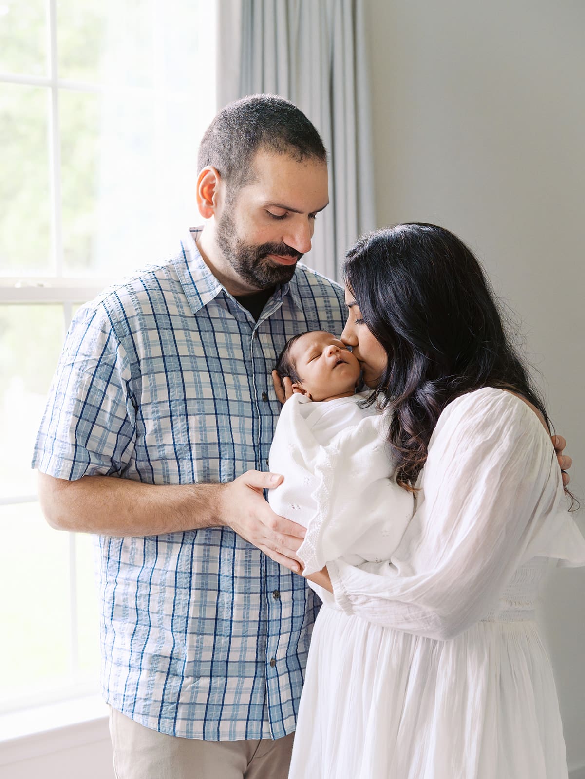 A mom kissing her baby as dad looks at them during a session by Katie Stansfield Photographer, a Chesterfield Newborn Photographer.