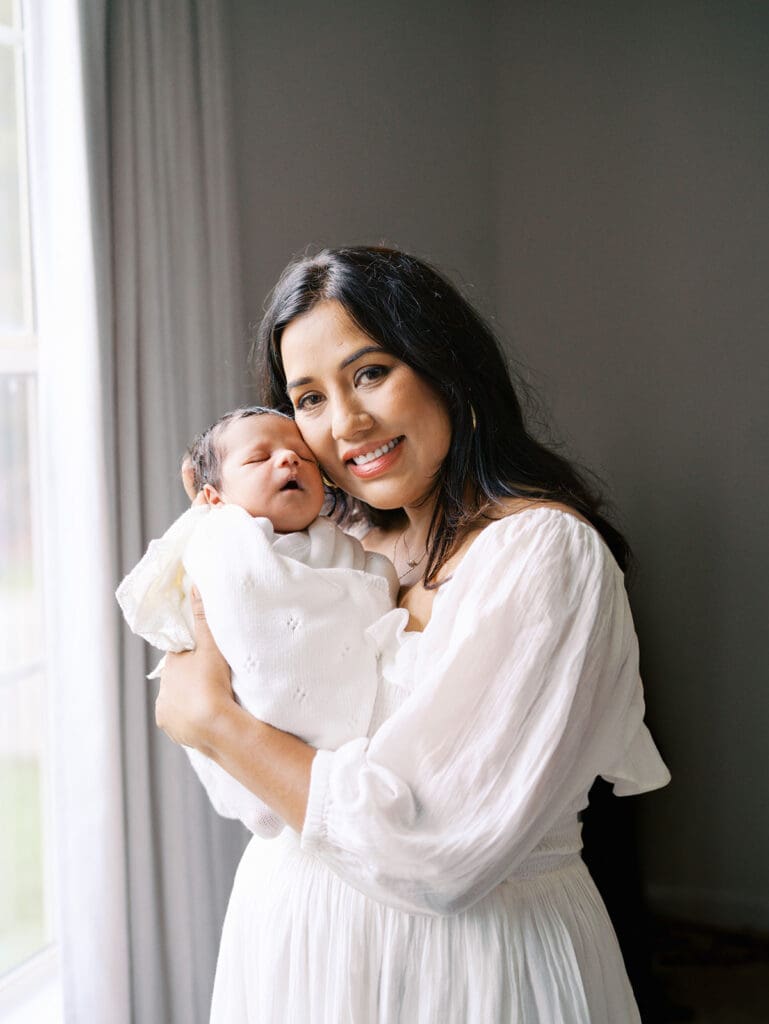 A mom smiling while holding up her baby during a session by Katie Stansfield Photography, a Chesterfield Newborn Photographer.