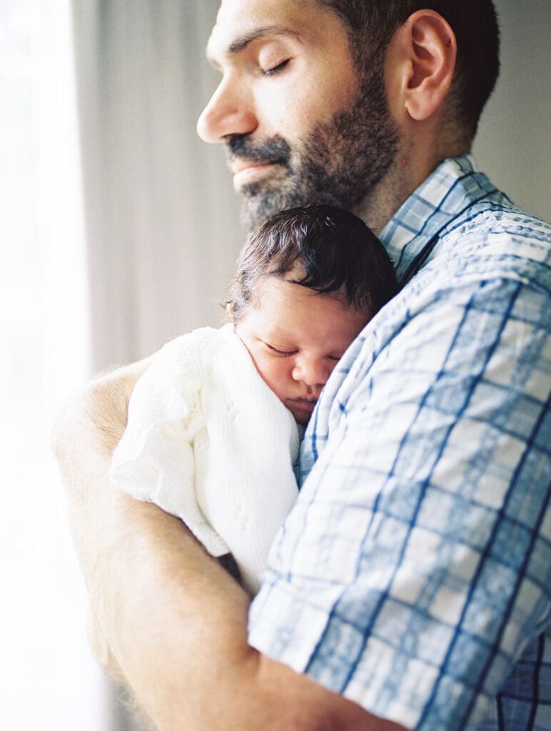 A dad holding his baby against his chest during a session by Katie Stansfield Photography, a Chesterfield Newborn Photographer.