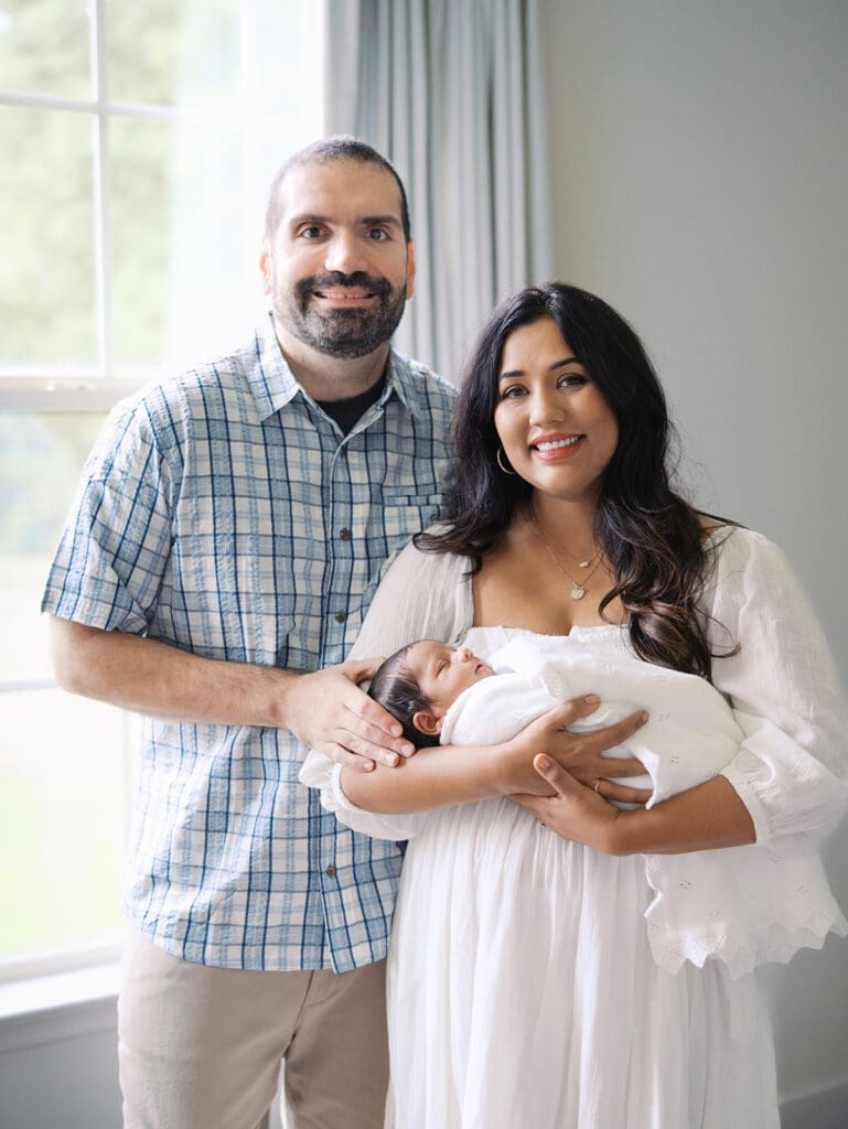 A mom and dad smiling as mom holds their baby during a session by Katie Stansfield Photography, a Chesterfield Newborn Photographer.