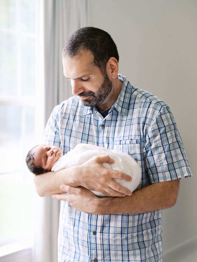 A dad holding and looking down at his baby during a session by Katie Stansfield Photography, a Chesterfield Newborn Photographer.