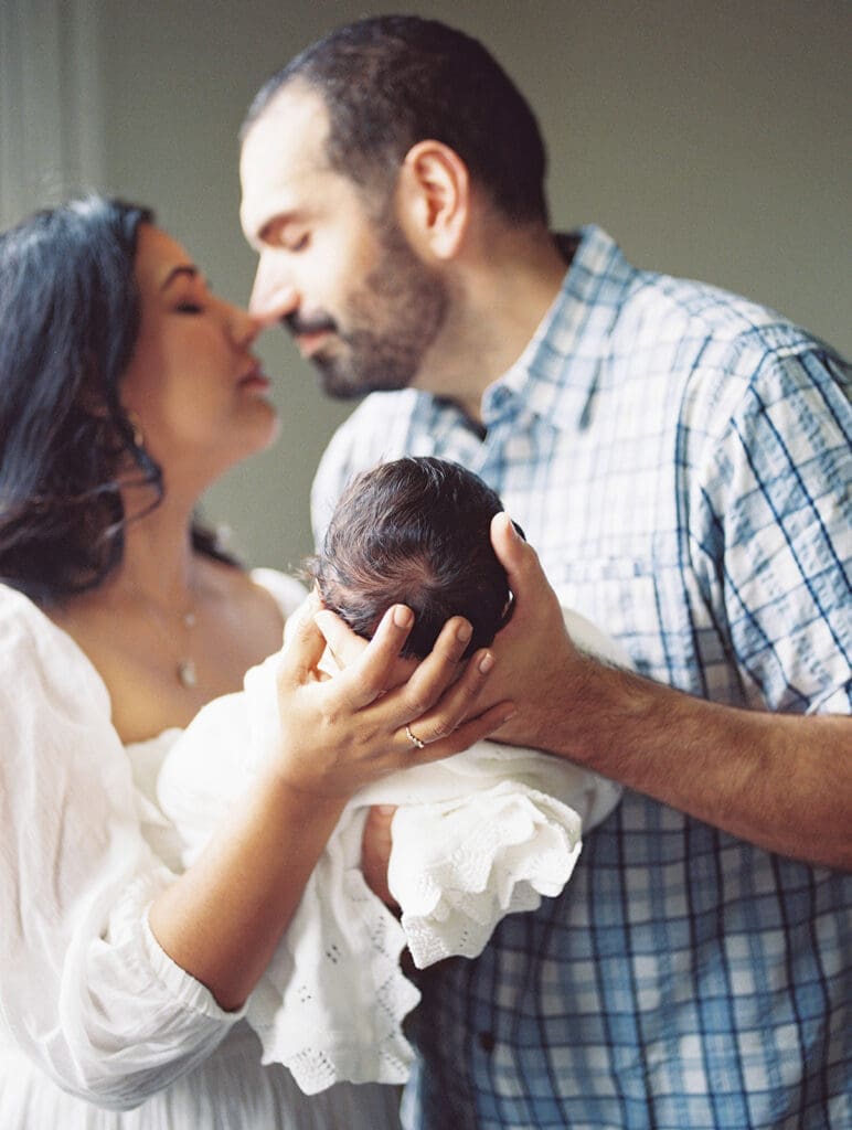 A mom and dad touching noses while holding their baby during a session by Katie Stansfield Photography, a Chesterfield newborn photographer.