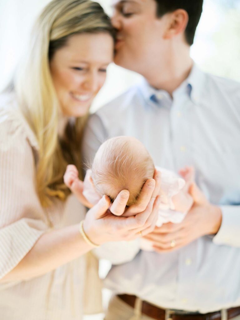 A mom and dad holding their baby as dad kisses mom's temple at a newborn session by Katie Stansfield Photography.