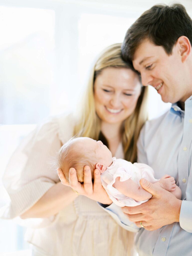 A mom and dad smiling at their baby at the best time of day for newborn photos by Katie Stansfield Photography.