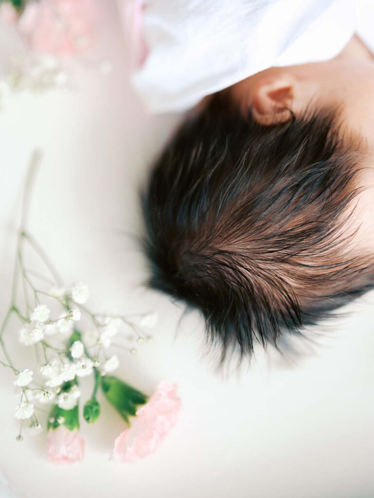 A close-up of a baby's head of hair next to flowers at an in-home session by Katie Stansfield Photography, a Midlothian newborn photographer.