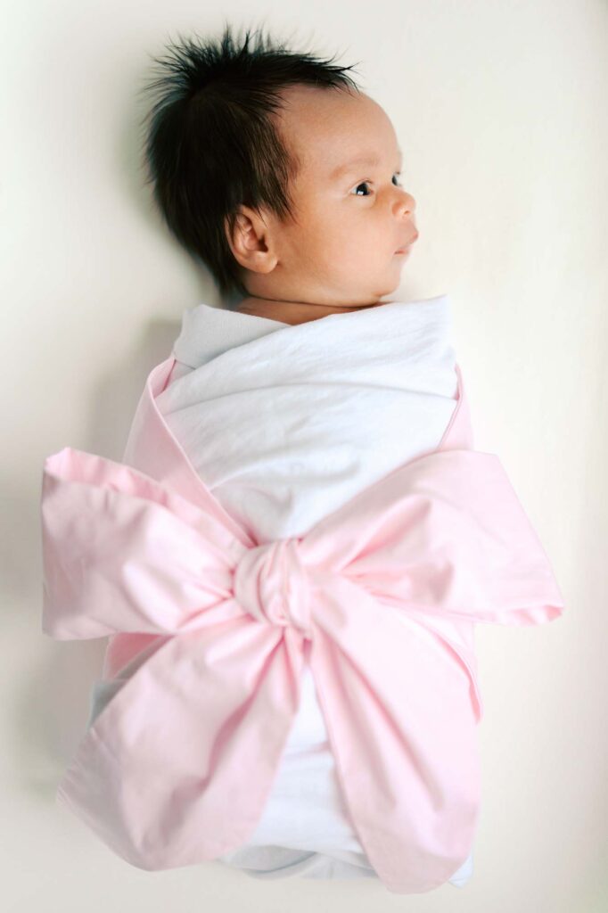 A baby in a pink bow-wrapped swaddle at an in-home session by Katie Stansfield Photography.