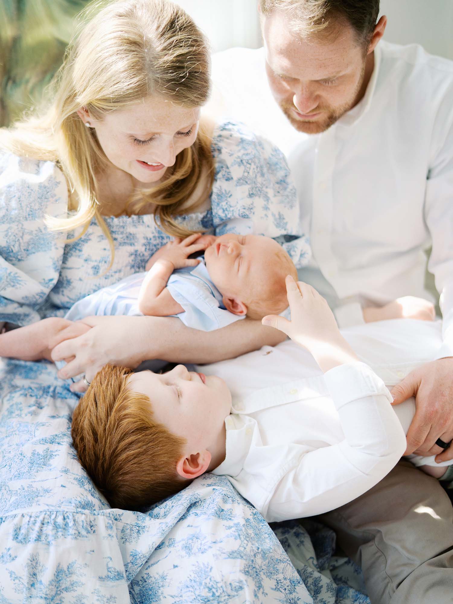 A young boy laying on his parents while playing with his baby brother by Katie Stansfield Photography, an Ashland VA newborn photographer.
