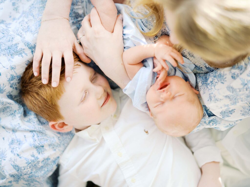 A close-up of a young boy laying next to his brother who is held in mom's arms at a newborn session by Katie Stansfield Photography.