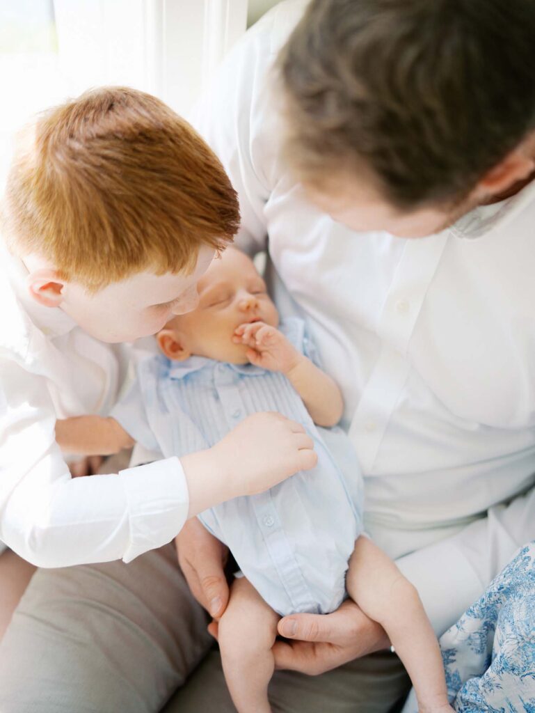 A young boy tickling his baby brother who is held in dad's arms by Katie Stansfield Photography, an Ashland VA newborn photographer.