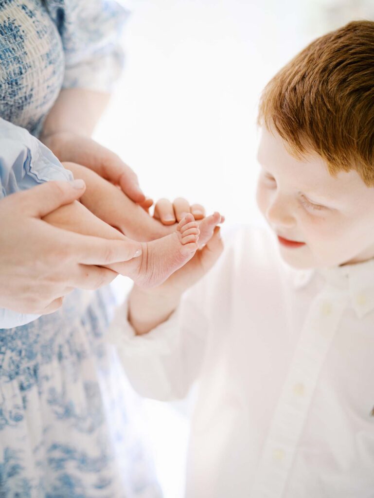 A close-up of a young boy playing with his baby brother's feet by Katie Stansfield Photography, an Ashland VA newborn photographer.