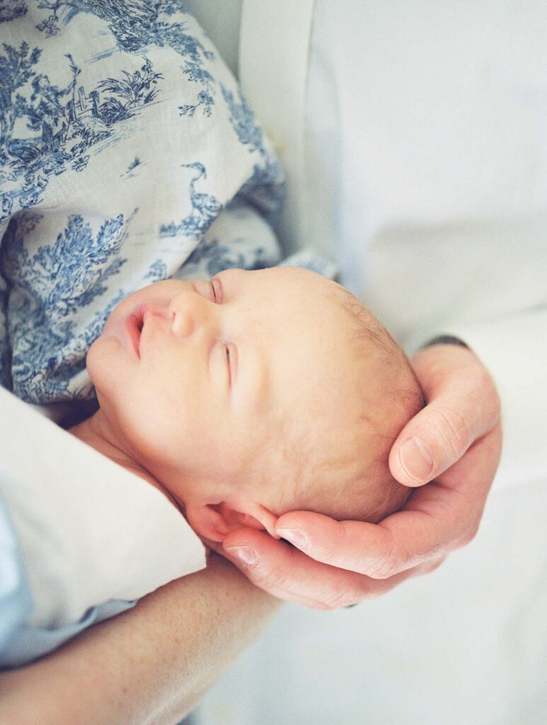 A close-up of a dad's hand holding a baby's head at a newborn session by Katie Stansfield Photography.
