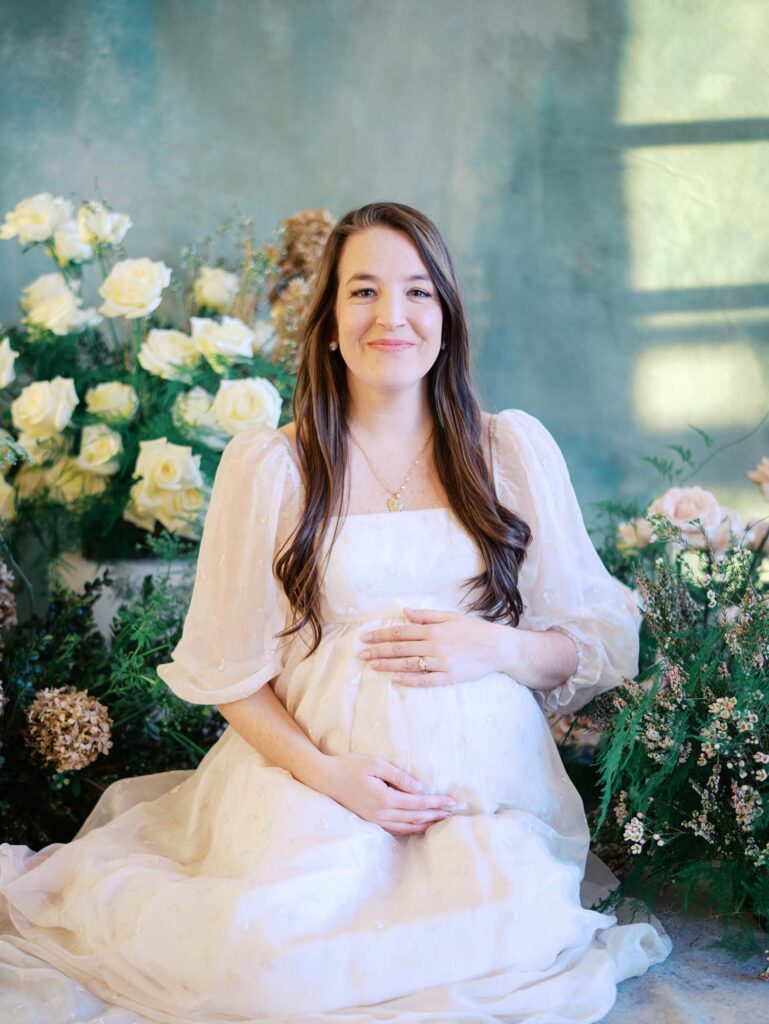 A mom surrounded by flowers holding her bump and smiling at a maternity photography session by Katie Stansfield Photography.