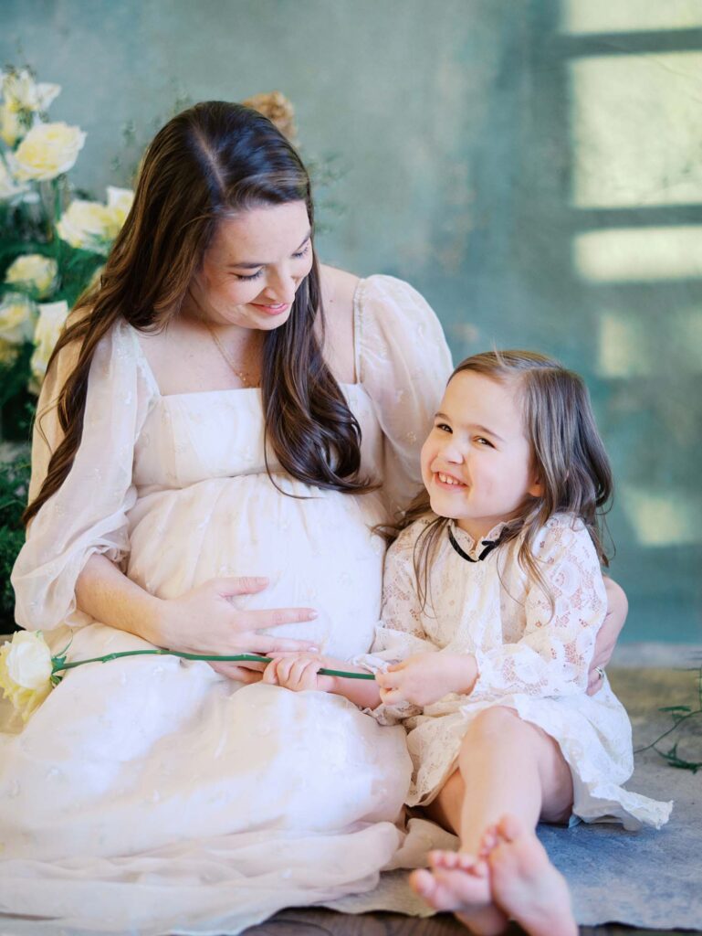A mom holding her baby bump and looking at her daughter as her daughter smiles at a maternity session by Katie Stansfield Photography, a Bon Air maternity photographer.