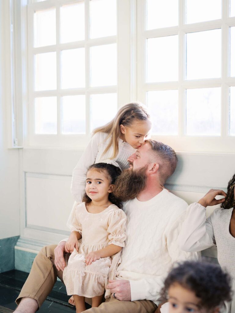 A daughter kissing her dad's head as another daughter smiles at a family session by Katie Stansfield Photography, a Richmond photographer.