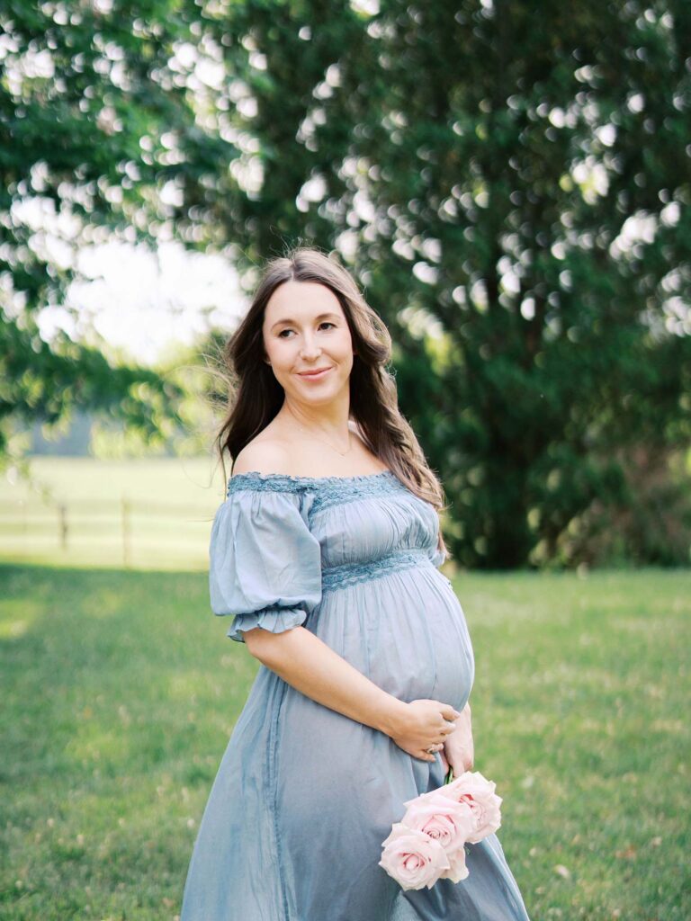 A mom smiling and holding her baby bump at a maternity photoshoot by Katie Stansfield Photography.
