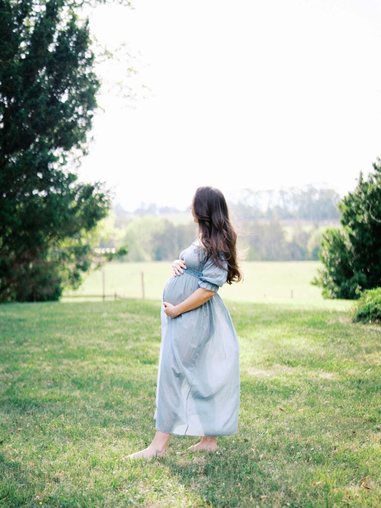 A mom holding her baby bump and looking into a field at a maternity session by Katie Stansfield Photography.