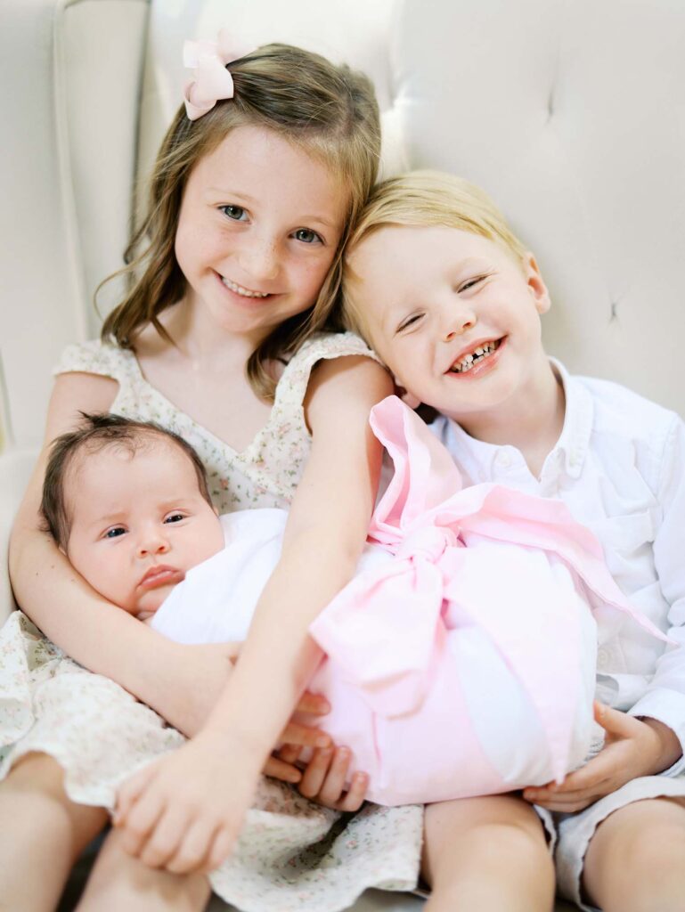 A brother and sister holding their baby sister in their home, one of the newborn photo locations in Richmond VA, by Katie Stansfield Photography.
