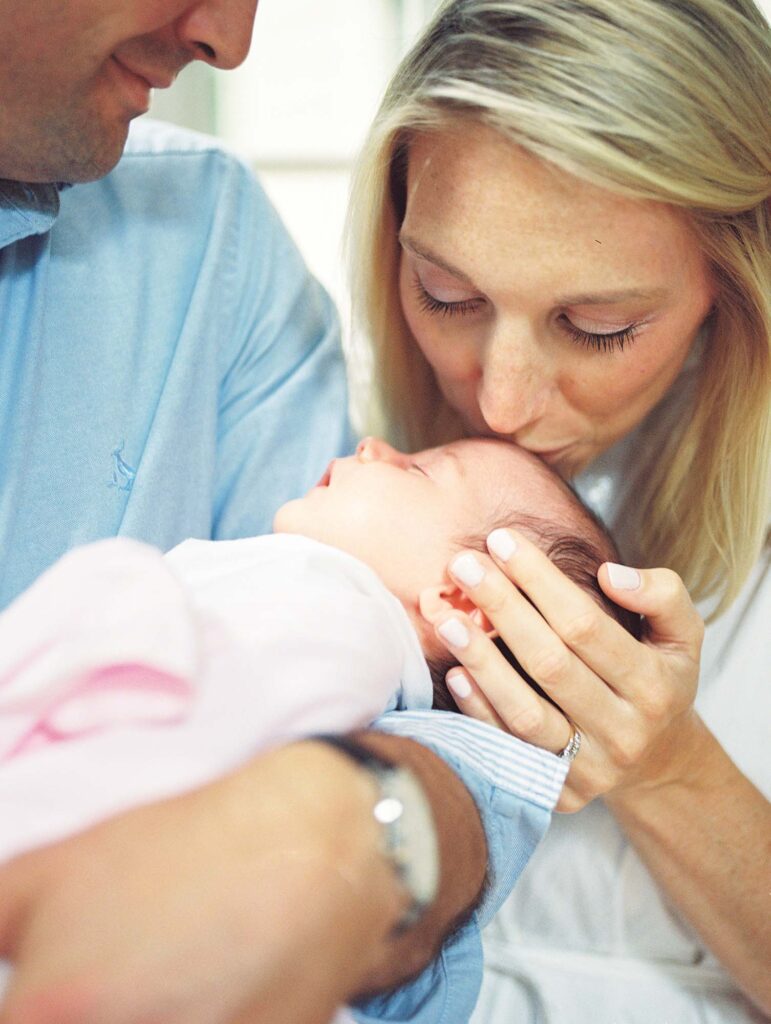 A close-up of dad holding a baby as mom kisses baby's head by Katie Stansfield Photography.
