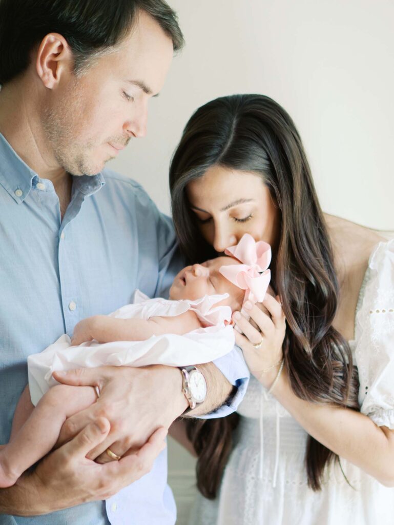 A dad holding a newborn as mom kisses the newborn at a newborn session by Katie Stansfield Photography.