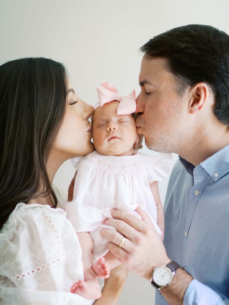 A mom and dad kissing a baby's cheeks by Katie Stansfield Photography, a Bon Air newborn photographer.