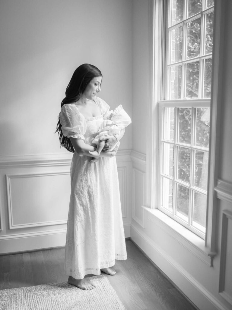 A mom holding and looking down at her baby by a window by Katie Stansfield Photography, a Bon Air newborn photographer.
