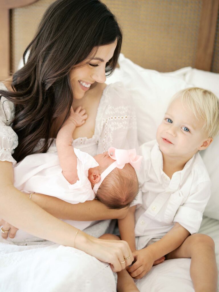A mom holding a baby and smiling at her toddler as the toddler smiles by Katie Stansfield Photography, a Bon Air newborn photographer.
