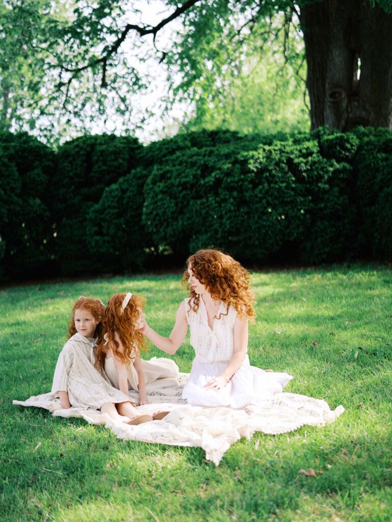 A mom and her two daughters sitting on a blanket as mom touches a daughter's face by Katie Stansfield Photography, a family photographer in Short Pump VA.