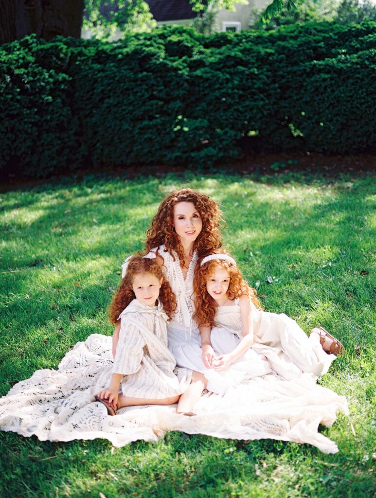 A mom and her two daughters sitting on a blanket and smiling at a family session by Katie Stansfield Photography.