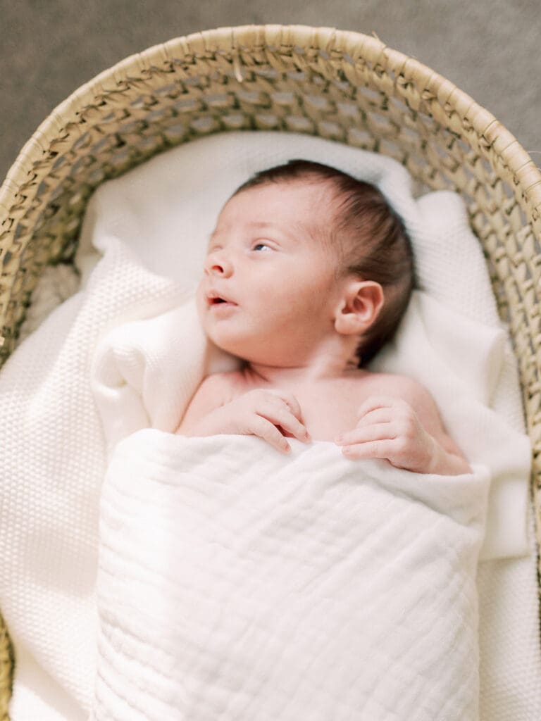 A baby looking to his right while wrapped in a blanket and laying in a basket at a Richmond in-home newborn photography session by Katie Stansfield Photography.