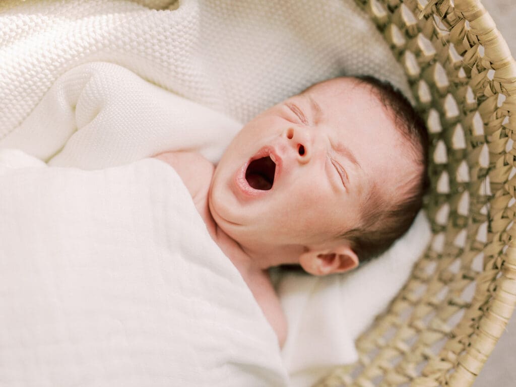 A baby yawning while laying in a basket at a Richmond in-home newborn photography session by Katie Stansfield Photography.