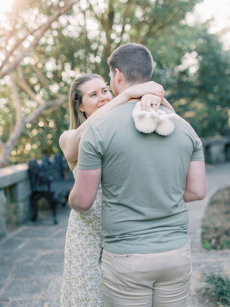 A man and woman looking at each other while the woman holds baby slippers at a maternity photography in Virginia session by Katie Stansfield Photography.
