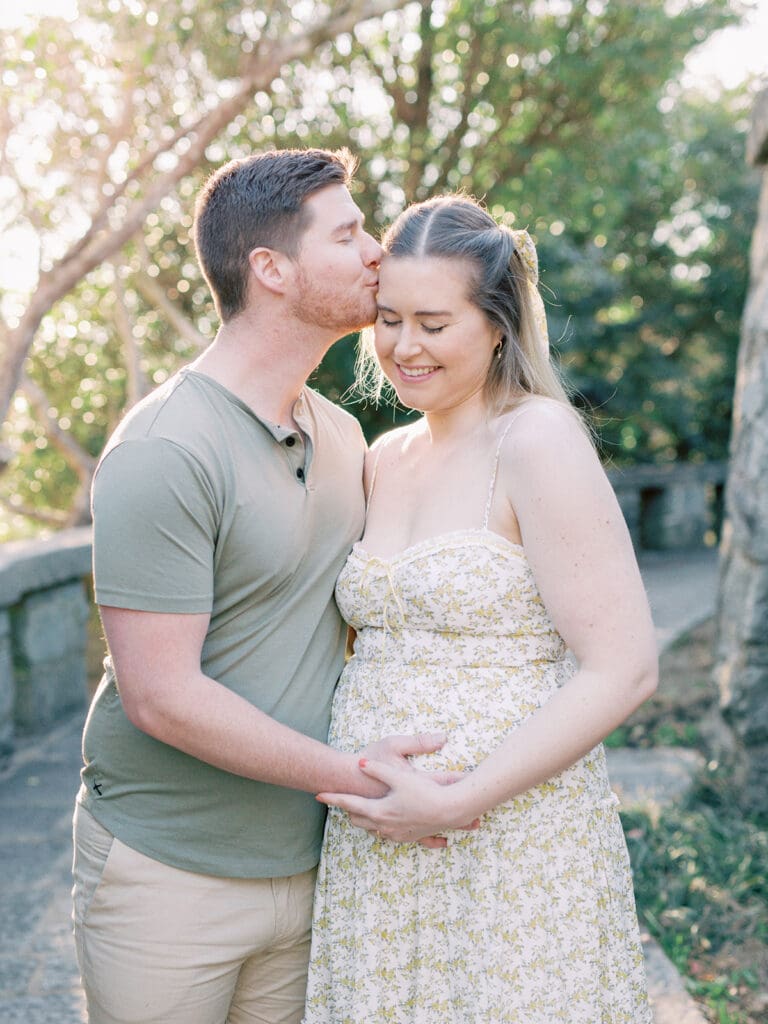 A man kissing a woman's temple while holding the woman's pregnancy bump at a maternity photography in Virginia session by Katie Stansfield Photography.