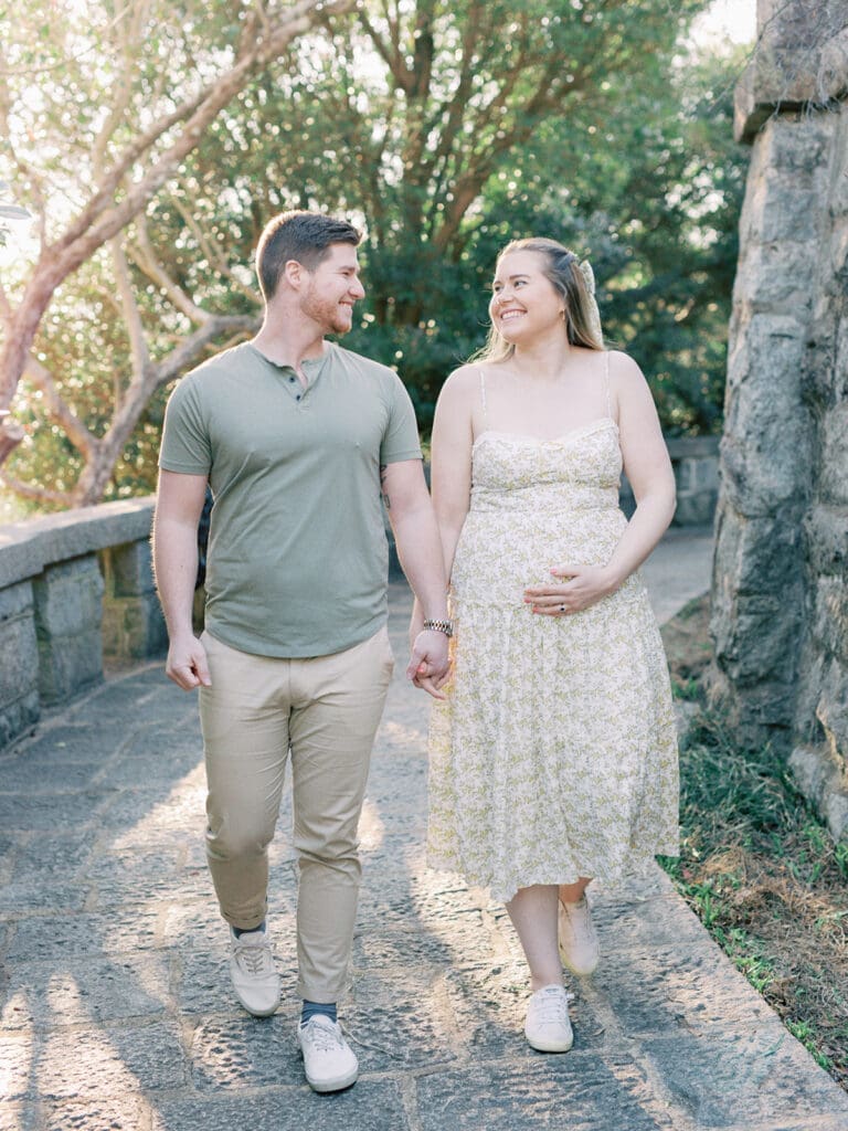 A man and woman walking while looking at each other with the woman holding her pregnancy bump during a Richmond maternity photography session by Katie Stansfield Photography.