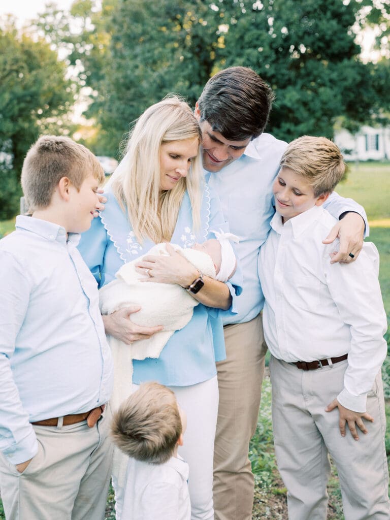 A mother holding her newborn while alongside her family at an outdoor newborn photography in Virginia session by Katie Stansfield Photography.
