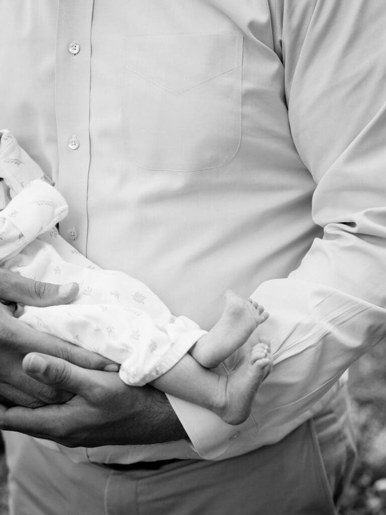 A close-up of a newborn's feet as the newborn is being held by the dad at an outdoor newborn photography in Virginia session by Katie Stansfield Photography.