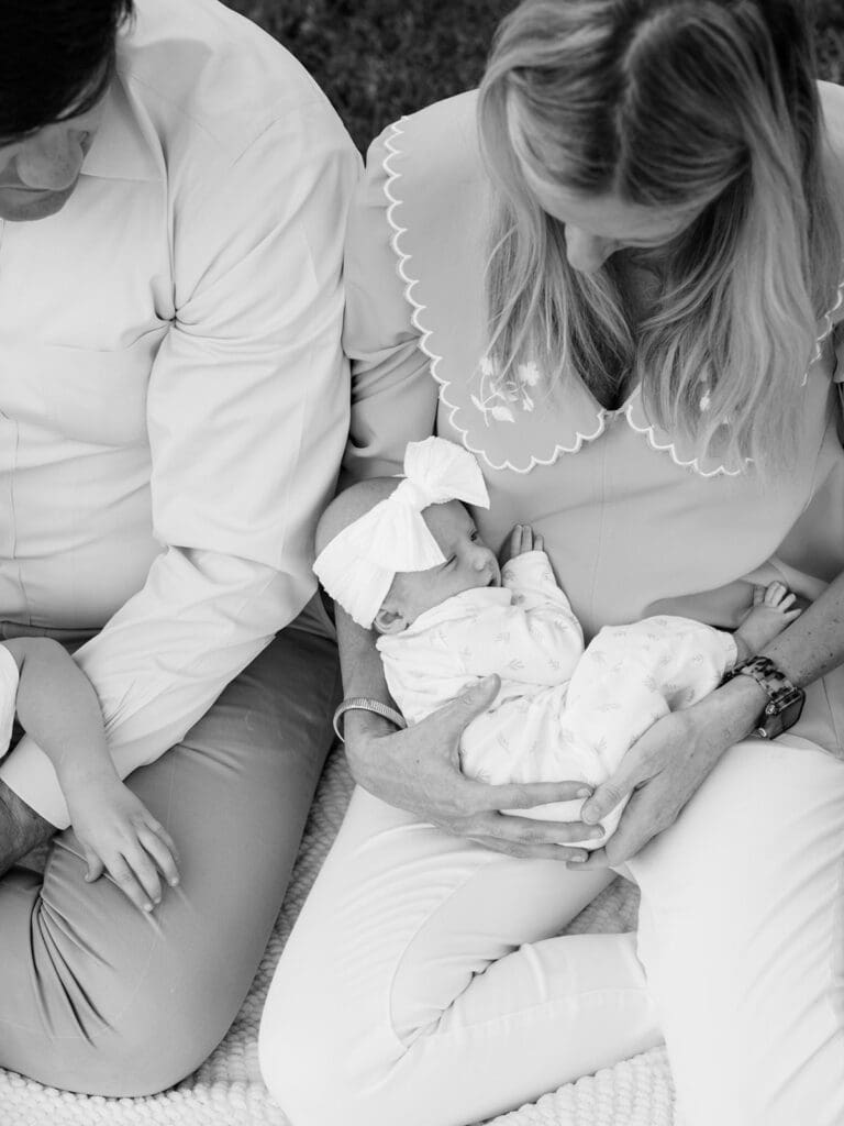 A mother holding her newborn while sitting next to the father at an outdoor newborn photography in Virginia session by Katie Stansfield Photography.