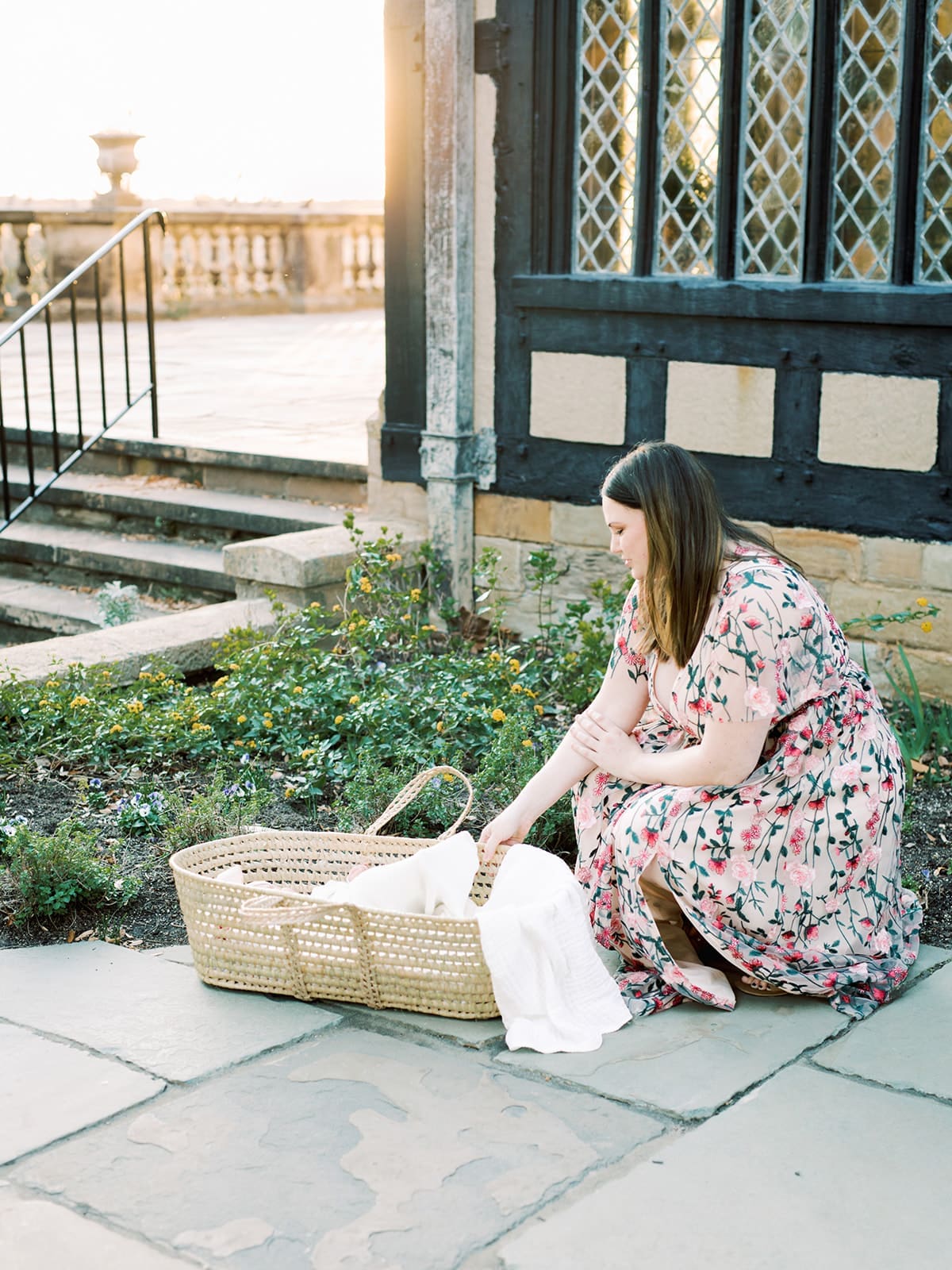 A woman bending down to hold a basket while looking down at her baby in the basket at a Richmond family photography session by Katie Stansfield Photography.