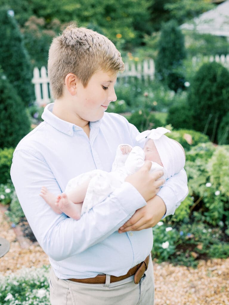 A young boy holding a newborn at an outdoor newborn photography session in Richmond by Katie Stansfield Photography.