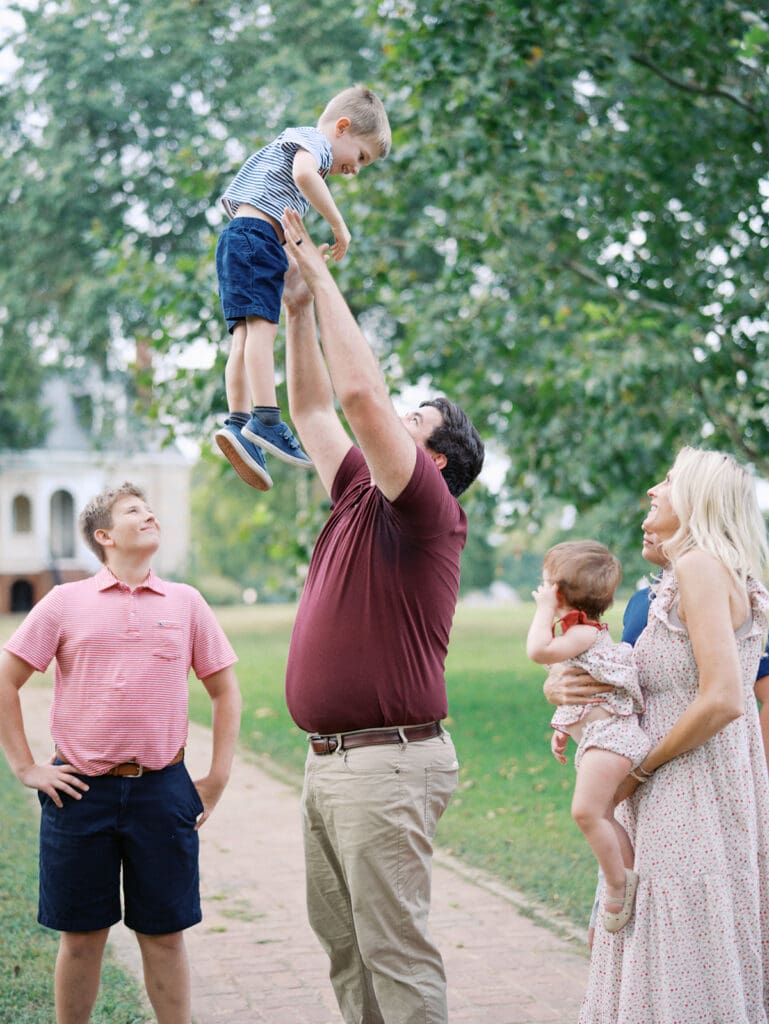 A dad holding up his child surrounded by their family at a Richmond fall mini session by Katie Stansfield Photography.
