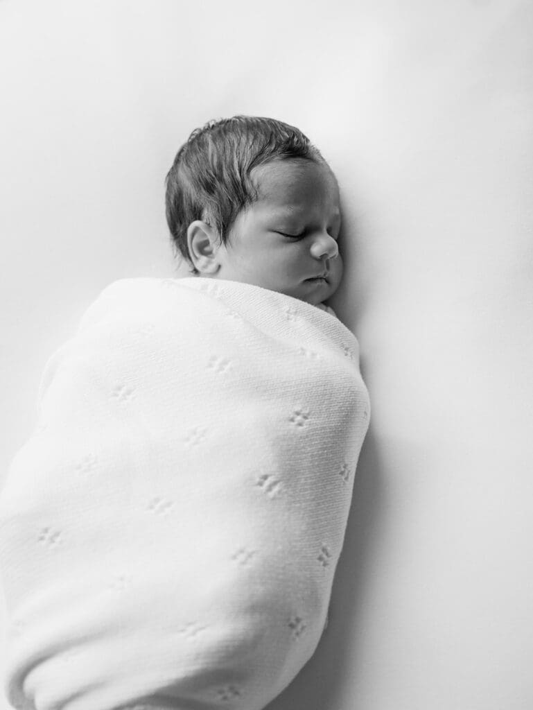 A baby sleeping while wrapped in a blanket during a newborn photography session in Richmond, Virginia by Katie Stansfield Photography.