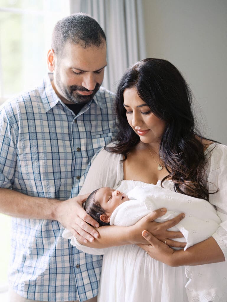 A mom holding a baby as mom and dad both look down at the baby during a newborn photography session in Richmond, Virginia by Katie Stansfield Photography.