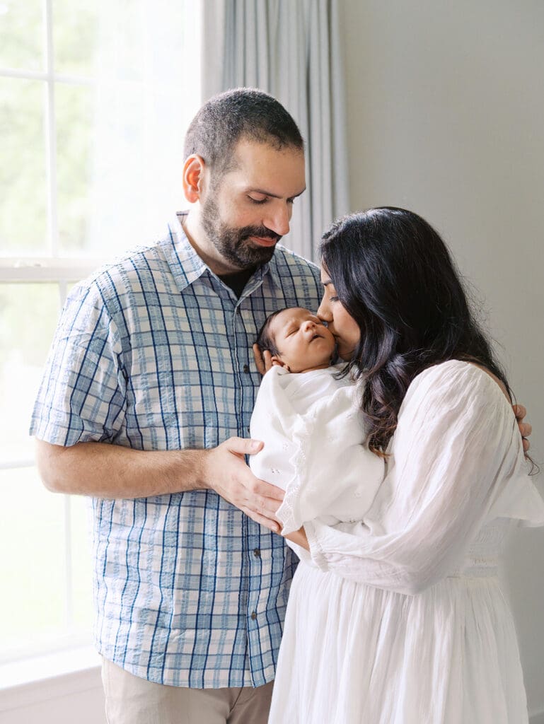 A mom kissing her baby as dad looks at them during a session by Katie Stansfield Photography, a Chesterfield Newborn Photographer.
